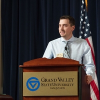 A man standing at a GVSU podium, speaking to the crowd